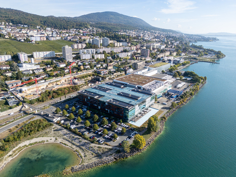 Aerial view of the Philip Morris RD Cube situated on the shore of Lake Neuchatel surrounded by parking areas urban development and lush greenery in Neuchatel Neuenburg Switzerland.