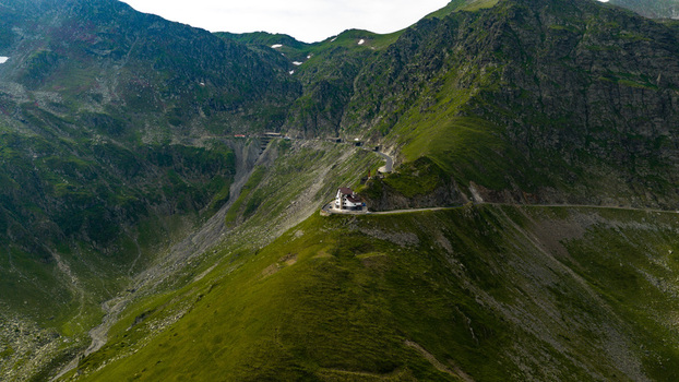 Aerial view of the winding Transfagarasan road cutting through the lush green Carpathian Mountains with a mountain lodge perched on the ridge in Curtea de Arges Judetul Arges Romania.