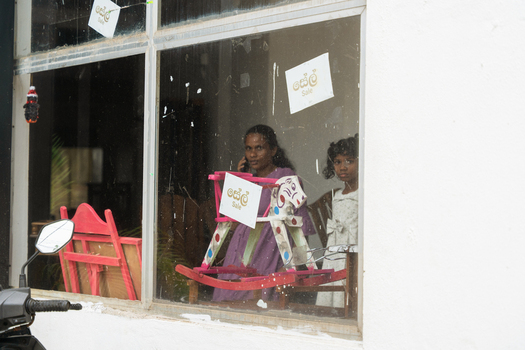 Sri Lanka 30 January 2026 View of a woman and a young girl looking out from a shop window featuring a wooden rocking horse and sale signs.