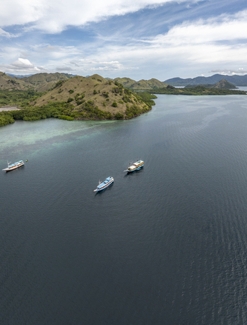 Aerial view of traditional boats sailing in the turquoise waters near the hilly landscape of Komodo Island in Komodo East Nusa Tenggara Indonesia. Aerial view of traditional boats sailing in the turquoise waters near the hilly landscape of Komodo Island in Komodo East Nusa Tenggara Indonesia.