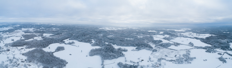 Aerial view of a vast snow covered landscape with dense forests and open fields under a cloudy winter sky in Latvia. Aerial view of a vast snow covered landscape with dense forests and open fields under a cloudy winter sky in Latvia.