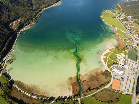 Aerial view of Achen Lake with turquoise waters surrounding green mountains and shoreline buildings in Schwaz District Tyrol Austria.