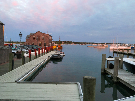 View of the harbor at dusk with wooden docks boats moored in the water and historic shingle style buildings under a soft pink and blue sky Edgartown Massachusetts United States.