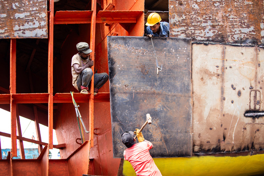 Keraniganj Bangladesh 04 September 2024 View of workers repairing a large vessel at the Shipyard Dhaka with one man using a hammer on a metal plate while others observe from the scaffolding.