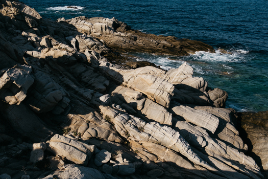 View of rugged coastal rock formations meeting the deep blue Aegean Sea Neos Marmaras Greece.