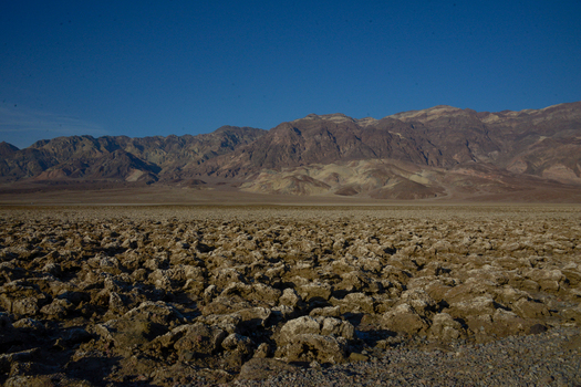 View of Devil s Golf Course with its jagged salt formations and distant mountains under a clear blue sky in Death Valley California United States.