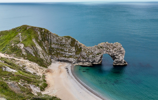 Aerial view of Durdle Door a natural limestone arch on the Jurassic Coast with turquoise waters sandy beach and grassy cliffs in Wareham England United Kingdom. Aerial view of Durdle Door a natural limestone arch on the Jurassic Coast with turquoise waters sandy beach and grassy cliffs in Wareham England United Kingdom.