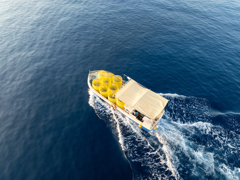 Aerial view of a boat carrying yellow containers cuts through the deep blue sea leaving a frothy white wake behind Ghajnsielem gozo Malta. Aerial view of a boat carrying yellow containers cuts through the deep blue sea leaving a frothy white wake behind Ghajnsielem gozo Malta.