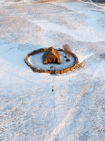 Aerial view of Grafarkirkja a historic turf church surrounded by a circular stone wall in a snow covered landscape with a person walking towards the entrance in Hofsos Skagafjordur Iceland. Aerial view of Grafarkirkja a historic turf church surrounded by a circular stone wall in a snow covered landscape with a person walking towards the entrance in Hofsos Skagafjordur Iceland.