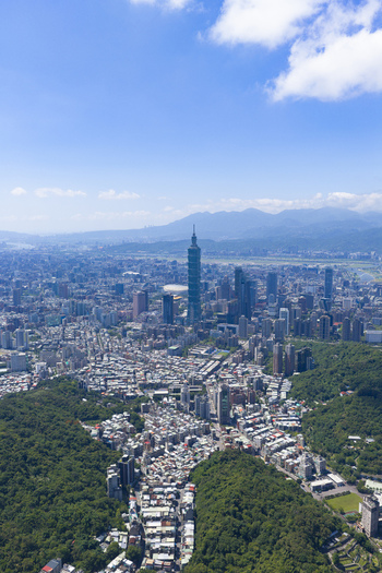 Aerial view of Taipei 101 skyscraper rising above the dense urban landscape surrounded by lush green hills residential rooftops and a clear blue sky Taipei City Taiwan. Aerial view of Taipei 101 skyscraper rising above the dense urban landscape surrounded by lush green hills residential rooftops and a clear blue sky Taipei City Taiwan.