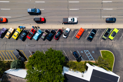 Birmingham United States 19 August 2023 Aerial view of classic and modern cars parked in a row at Woodward dream cruise car show with people walking nearby and a road with passing vehicles.