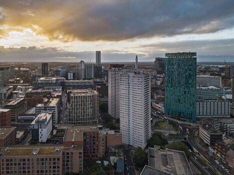 Aerial view of the Birmingham city skyline featuring modern skyscrapers residential towers and urban architecture under a dramatic golden hour sky in Birmingham England United Kingdom.