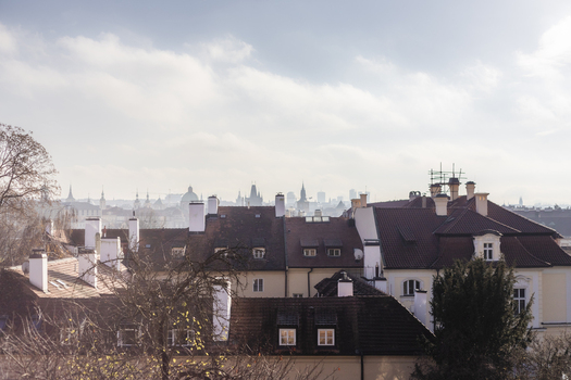 View of historic red tiled rooftops and white chimneys with the city skyline and spires under a soft cloudy sky in Prague Prague Czechia. View of historic red tiled rooftops and white chimneys with the city skyline and spires under a soft cloudy sky in Prague Prague Czechia.