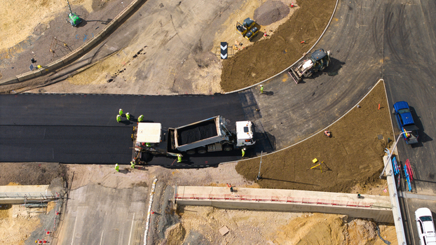 Aerial view of Black Cat Roundabout construction with workers paving fresh asphalt using heavy machinery and a dump truck in Chawston England United Kingdom. Aerial view of Black Cat Roundabout construction with workers paving fresh asphalt using heavy machinery and a dump truck in Chawston England United Kingdom.