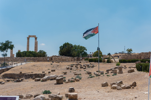 View of Amman Citadel with the Jordanian flag flying over ancient stone ruins and columns under a clear blue sky in Amman Amman Governorate Jordan.