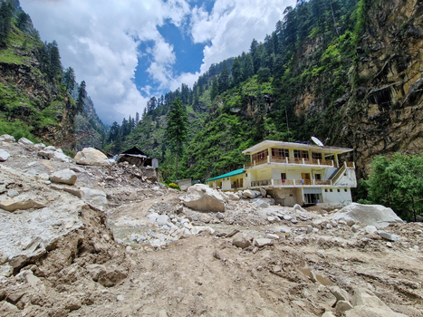 View of the village of Malana nestled in a mountainous valley in Himachal Pradesh India featuring a building surrounded by debris from a landslide.