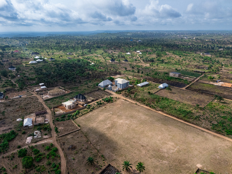 Aerial view of a sprawling rural landscape with scattered buildings a vast sun drenched field and lush green vegetation under a cloudy sky Elu Abia Nigeria. Aerial view of a sprawling rural landscape with scattered buildings a vast sun drenched field and lush green vegetation under a cloudy sky Elu Abia Nigeria.