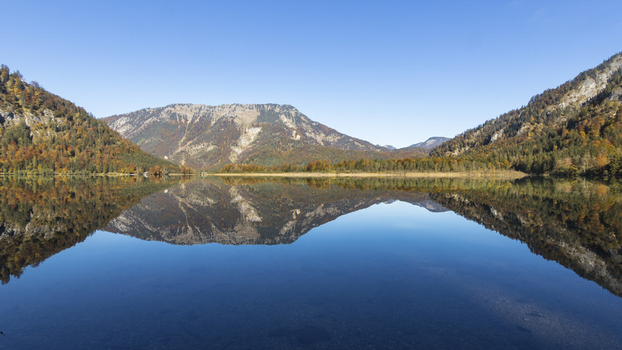 View of Offensee lake reflecting the surrounding mountains and autumn foliage under a clear blue sky in Ebensee Upper Austria Austria. View of Offensee lake reflecting the surrounding mountains and autumn foliage under a clear blue sky in Ebensee Upper Austria Austria.