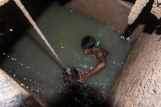 Dhaka Bangladesh 18 April 2018 View of a manual sewer cleaner submerged in murky water inside a dark brick shaft while holding a bucket attached to a rope. Dhaka Bangladesh 18 April 2018 View of a manual sewer cleaner submerged in murky water inside a dark brick shaft while holding a bucket attached to a rope.