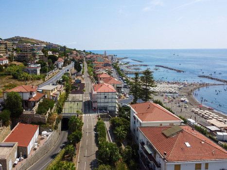 Aerial view of the coastal town featuring red tiled rooftops a road with a tunnel a sandy beach with umbrellas and people and the blue Mediterranean Sea in San Lorenzo Liguria Italy.