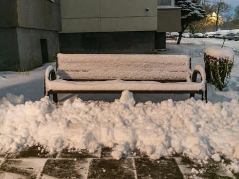 View of a wooden bench covered in a thick layer of fresh snow situated in a residential area with snow covered ground and a parking lot in Vilnius Vilnius County Lithuania. View of a wooden bench covered in a thick layer of fresh snow situated in a residential area with snow covered ground and a parking lot in Vilnius Vilnius County Lithuania.