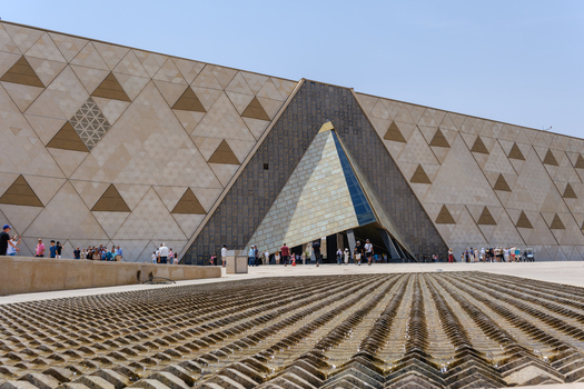 Giza Egypt 16 May 2026 View of the Grand Egyptian Museum featuring its modern triangular facade and entrance with tourists walking in the plaza.