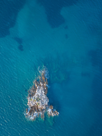 Aerial view of a small rocky island surrounded by deep blue sea in Albania.