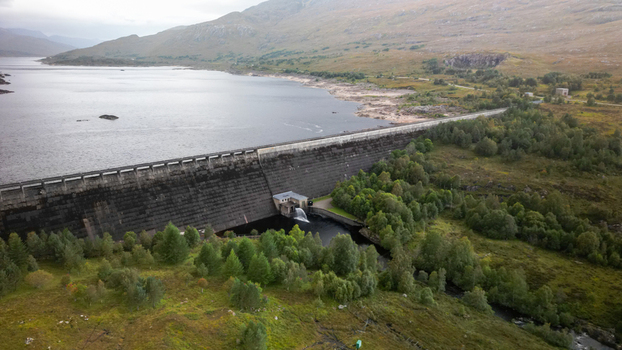 Aerial view of Cluanie Dam holding back the waters of Loch Cluanie surrounded by rugged hills and lush green vegetation in Inverness Scotland United Kingdom.