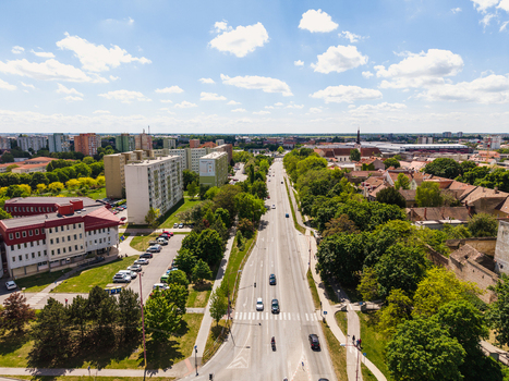 Aerial view of multi story apartment buildings and lush green trees along a wide city street under a blue sky with white clouds in Trnava Trnava Region Slovakia. Aerial view of multi story apartment buildings and lush green trees along a wide city street under a blue sky with white clouds in Trnava Trnava Region Slovakia.