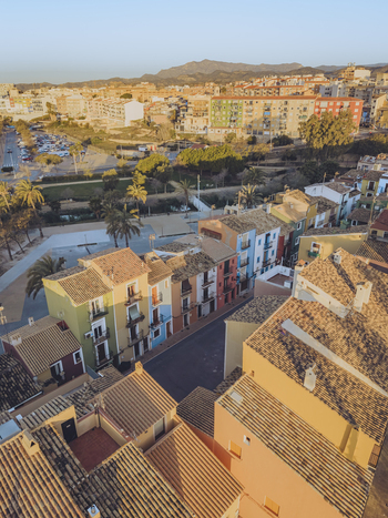 Aerial view of colorful houses with terracotta rooftops and palm trees under a clear sky in La Vila Joiosa Valencian Community Spain. Aerial view of colorful houses with terracotta rooftops and palm trees under a clear sky in La Vila Joiosa Valencian Community Spain.