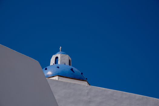 View of a traditional blue domed church with white walls under a clear blue sky in Fira Greece. View of a traditional blue domed church with white walls under a clear blue sky in Fira Greece.