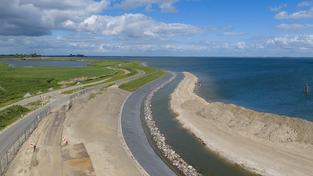 Aerial view of the dike reinforcement project along the coastline with a winding road green embankments and sandy construction works in Uitdam North Holland Netherlands.