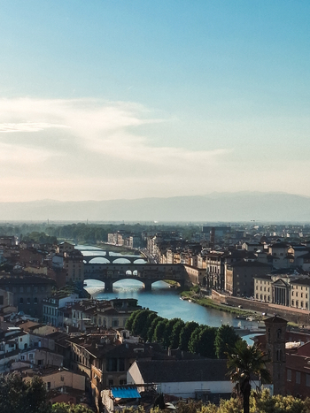 View of the historic Ponte Vecchio bridge spanning the Arno River with surrounding stone buildings and lush trees in Florence Tuscany Italy. View of the historic Ponte Vecchio bridge spanning the Arno River with surrounding stone buildings and lush trees in Florence Tuscany Italy.