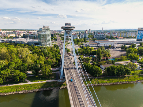 Aerial view of Most SNP bridge with its iconic UFO observation deck spanning the Danube river surrounded by lush green trees and the city skyline Bratislava Bratislava Region Slovakia. Aerial view of Most SNP bridge with its iconic UFO observation deck spanning the Danube river surrounded by lush green trees and the city skyline Bratislava Bratislava Region Slovakia.