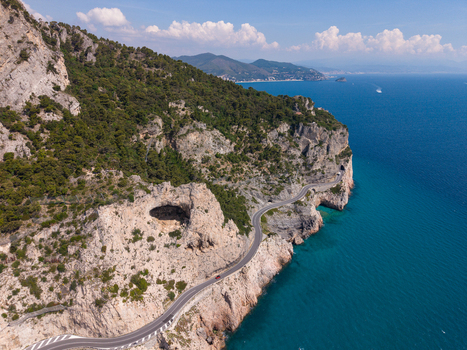 Aerial view of the Sentiero del Pellegrino area featuring the winding coastal road along steep limestone cliffs and the turquoise sea in Noli Liguria Italy.