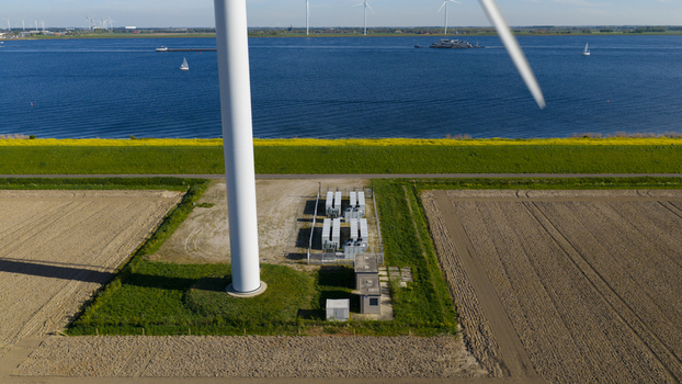 Aerial view of a wind turbine base and electrical infrastructure next to a green dike and blue water in Ooltgensplaat South Holland Netherlands. Aerial view of a wind turbine base and electrical infrastructure next to a green dike and blue water in Ooltgensplaat South Holland Netherlands.