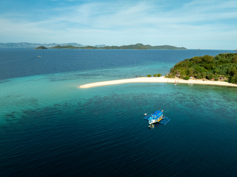 Aerial view of Malcapuya Island featuring a pristine white sand beach vibrant turquoise waters coral reefs and a traditional outrigger boat in Coron Mimaropa Philippines. Aerial view of Malcapuya Island featuring a pristine white sand beach vibrant turquoise waters coral reefs and a traditional outrigger boat in Coron Mimaropa Philippines.