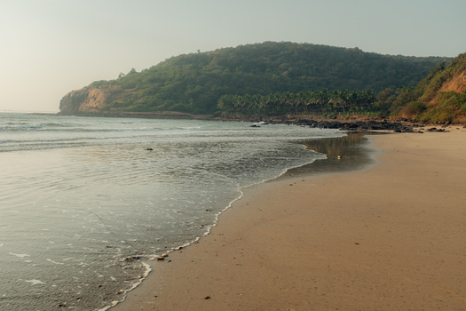 View of waves gently kissing the golden sands beneath a lush green crowned hill under a tranquil sky a serene coastal escape Chiplun Maharashtra India. View of waves gently kissing the golden sands beneath a lush green crowned hill under a tranquil sky a serene coastal escape Chiplun Maharashtra India.