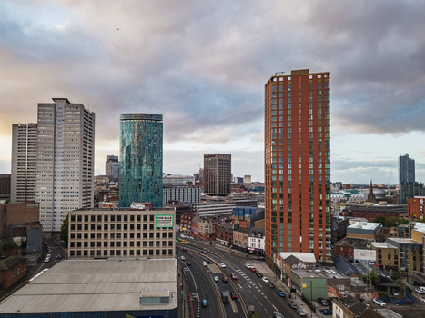 Aerial view of the Birmingham skyline featuring modern high rise buildings the iconic cylindrical Rotunda and urban roads under a cloudy sky in Birmingham England United Kingdom.