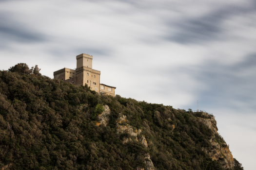 View of the historic Castello del Boccale perched on a rocky cliff surrounded by lush Mediterranean vegetation under a long exposure sky in Calafuria Toscana Italy.