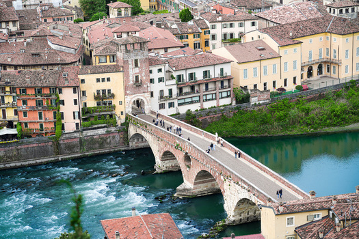 Aerial view of the historic Ponte Pietra bridge crossing the Adige River with people walking and traditional rooftops in Verona Veneto Italy.
