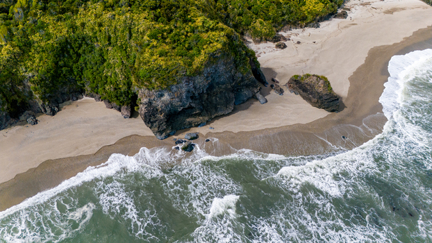 Aerial view of the rugged coastline where emerald forest meets sandy beach and foamy waves Ship Creek Haast West Coast Region New Zealand. Aerial view of the rugged coastline where emerald forest meets sandy beach and foamy waves Ship Creek Haast West Coast Region New Zealand.