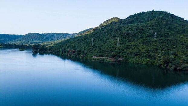 Aerial view of a wide river flowing past lush green hills with power transmission towers in Ghana. Aerial view of a wide river flowing past lush green hills with power transmission towers in Ghana.