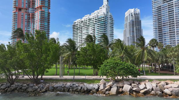 Aerial view of Miami Beach waterfront park with lush palm trees green lawns and modern high rise buildings along the rocky shoreline in Miami Beach Florida United States. Aerial view of Miami Beach waterfront park with lush palm trees green lawns and modern high rise buildings along the rocky shoreline in Miami Beach Florida United States.
