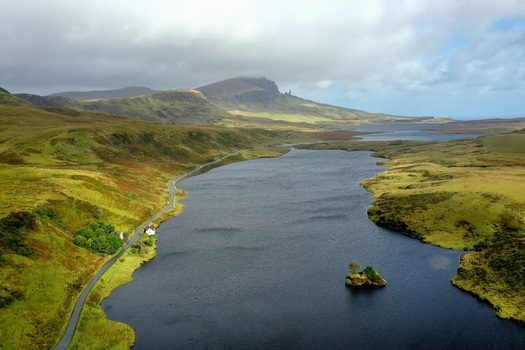 Aerial view of The Storr and Loch Fada with a winding road and green hills in the landscape of Portree Scotland United Kingdom.