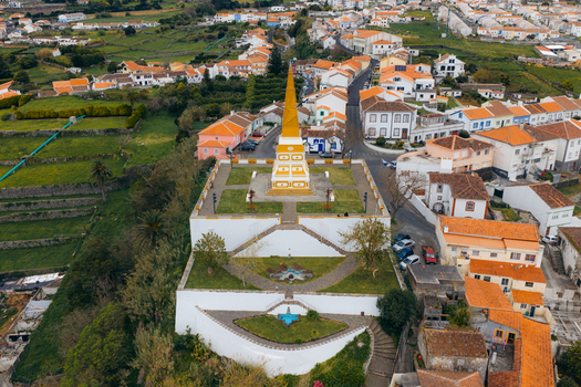 Aerial view of the Alto da Memoria obelisk with its yellow and white facade overlooking terraced gardens and the historic town of Angra do Heroismo Azores Portugal.
