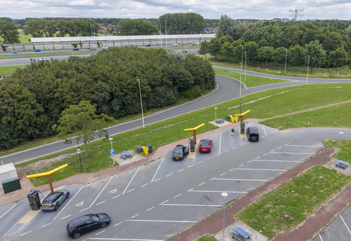 Aerial view of the Fastned charging station with electric vehicles parked at charging points surrounded by green landscape and a nearby highway in Breukelen Utrecht Netherlands. Aerial view of the Fastned charging station with electric vehicles parked at charging points surrounded by green landscape and a nearby highway in Breukelen Utrecht Netherlands.