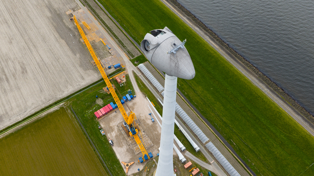 Aerial view of a wind turbine under construction with a large yellow crane turbine blades on the ground and agricultural fields near a waterway in Espel Flevoland Netherlands. Aerial view of a wind turbine under construction with a large yellow crane turbine blades on the ground and agricultural fields near a waterway in Espel Flevoland Netherlands.