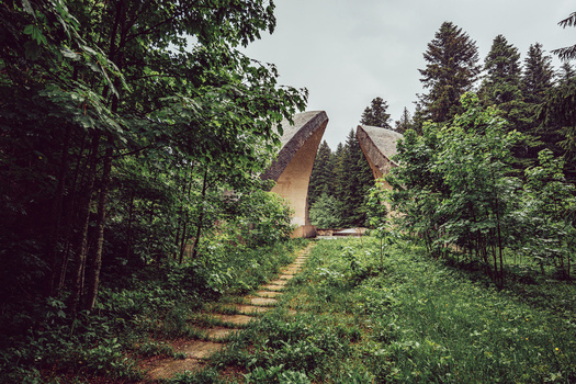 View of the Korcanica Memorial Zone monument surrounded by lush green forest and a stone path under a cloudy sky Sanski Most Federation of Bosnia Bosnia and Herzegovina. View of the Korcanica Memorial Zone monument surrounded by lush green forest and a stone path under a cloudy sky Sanski Most Federation of Bosnia Bosnia and Herzegovina.