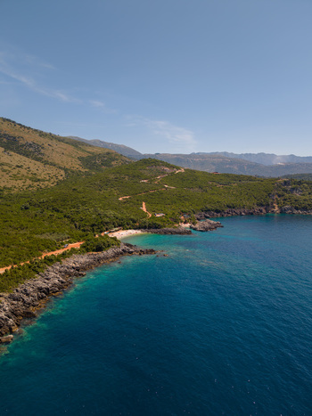 Aerial view of Aquarium Beach with turquoise sea rocky coastline and lush green hills in Jala Vlore County Albania.